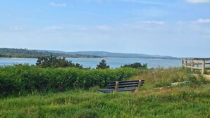 Un banc placé face à une étendue d’eau, avec une rive et des collines visibles au loin.