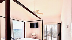 A bedroom with a four-poster bed, a ceiling fan, a TV, and a view of the outdoors. - East End Paradise Villas 4Bd3.5B-Private Beach-On the Water-w/ Sea Level Studio (East End)