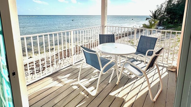 A covered outdoor seating area with a view of the ocean, a ceiling fan, and a table with chairs. - East End Paradise Villas 4Bd3.5B-Private Beach-On the Water-w/ Sea Level Studio (East End)