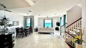 A spacious living area with a dining table, a sofa, and a view of the sea. - East End Paradise Villas 4Bd3.5B-Private Beach-On the Water-w/ Sea Level Studio (East End)