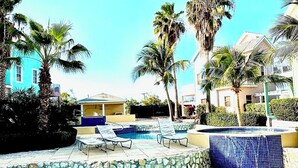 A swimming pool with lounge chairs, palm trees, and a stone-tiled edge. - East End Paradise Villas 4Bd3.5B-Private Beach-On the Water-w/ Sea Level Studio (East End)