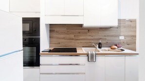 A modern kitchen with white cabinetry, a built-in oven, a microwave, a wooden backsplash, a sink, and a cutting board with a loaf of bread and a bottle of olive oil.