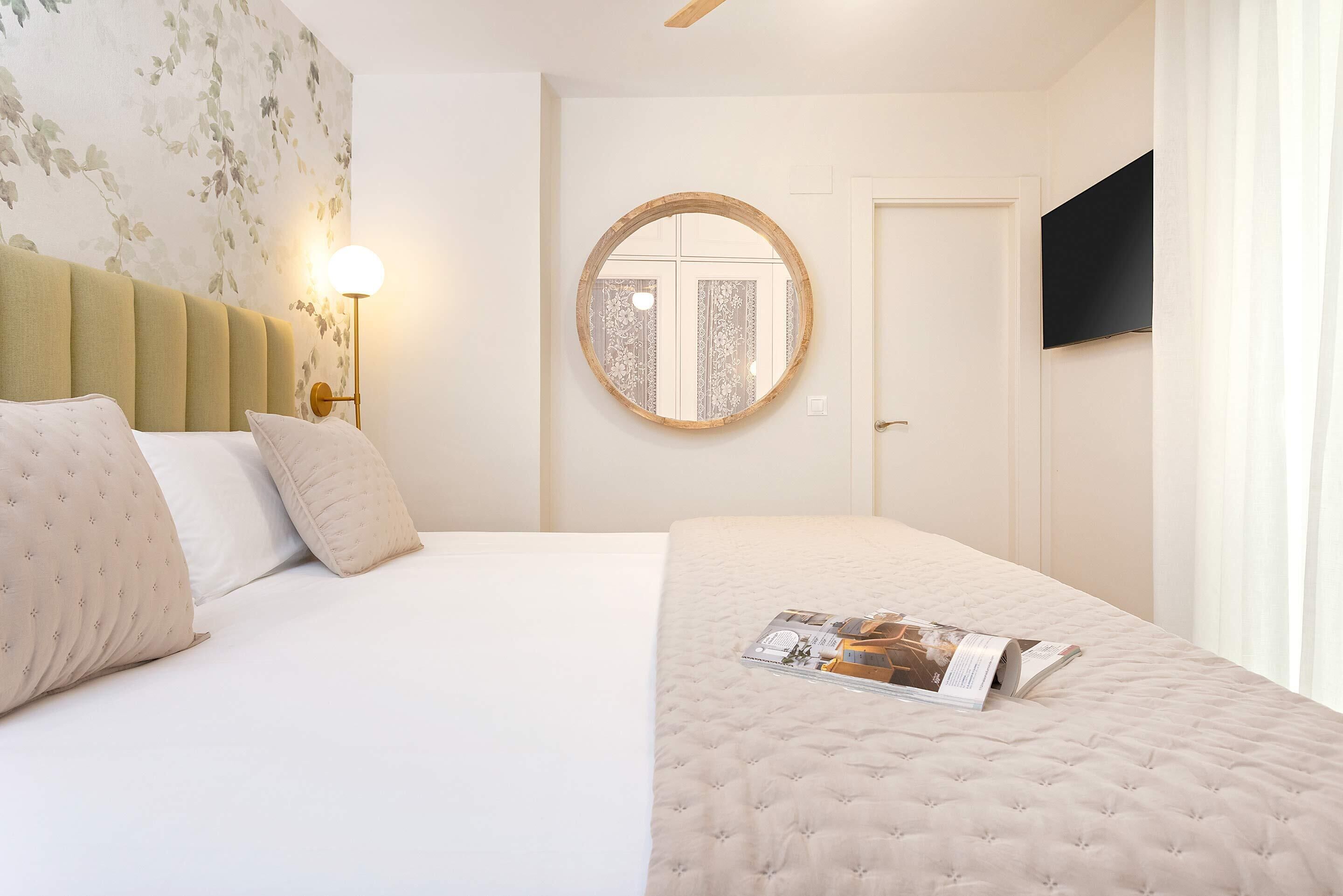 Ein Hotelzimmer mit einem Bett, einem runden Spiegel, einem Wand-Fernseher und einer Nachttischlampe.