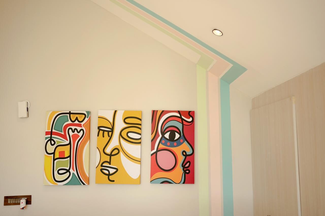 Three abstract paintings on a wall in a room with a wooden door and a light-colored ceiling.