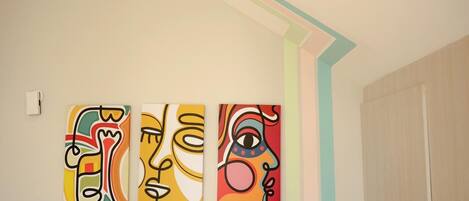 Three abstract paintings on a wall in a room with a wooden door and a light-colored ceiling.