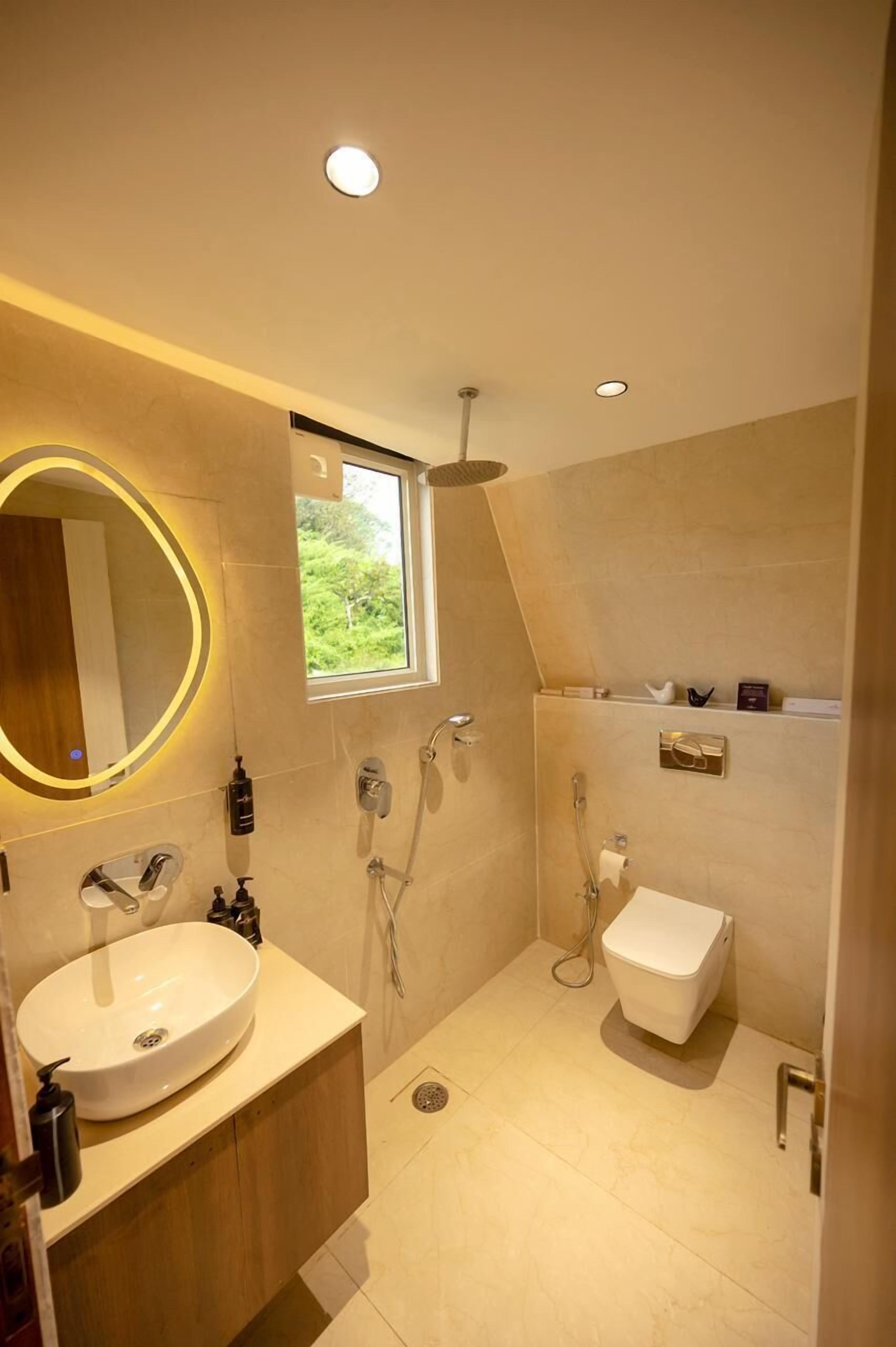 A modern bathroom with a large oval mirror, a sink, a toilet, and a shower.