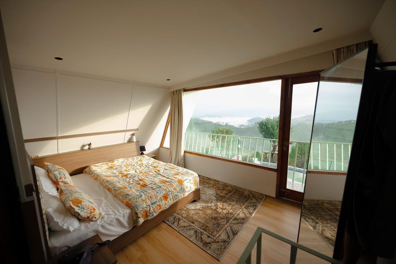 A bedroom with a bed, a large window, and a view of the outdoors.
