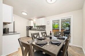 Una cocina moderna con armarios blancos, encimera negra y comedor con mesa de madera para seis comensales.