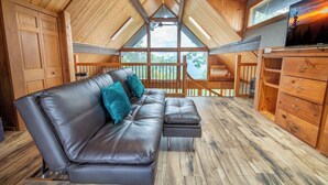 Un dormitorio estilo loft acogedor con techo de madera, un ventanal grande, un sofá de cuero y un aparador de madera.