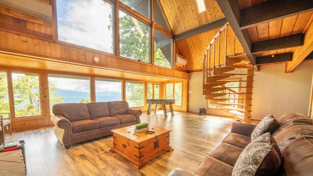 Un salón amplio con ventanas grandes, una escalera de madera y una zona de estar acogedora.
