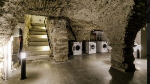 An underground laundry room with stone walls, a staircase leading up, and three washing machines. - Charming 1-bedroom apartment with WIFI in Old Tallinn (Tallinn)