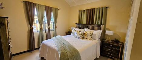 Quarto com cama, cortinas, mesa de cabeceira e cômoda.
