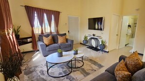 Un salon avec un canapé gris, deux petites tables rondes et un téléviseur à écran plat fixé au mur.