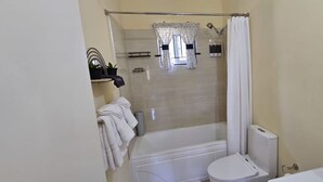 Une salle de bain équipée d’une baignoire, de toilettes et d’un espace douche séparé par une porte en verre.