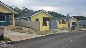 Une rangée de maisons jaunes aux toits gris, une route pavée et un paysage vallonné en arrière-plan.