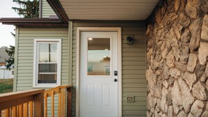 Una casa con una porta bianca, un piccolo portico con ringhiera in legno e un muro di pietra.