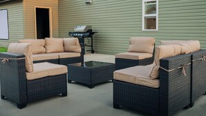 Una terrazza con mobili in vimini, un tavolo in vetro e un barbecue.