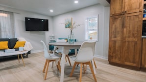 Un soggiorno moderno con zona pranzo, TV a schermo piatto e mobili contenitori in legno.
