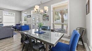 A modern dining area with a glass table, blue chairs, and a chandelier.