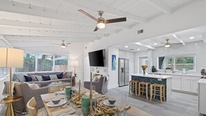 A spacious living area with a dining table set for a meal, a sofa, and a kitchen with a large island and bar stools. - 237 | Heated Pool | Putting | Outdoor Living | FreeBee Zone | by DelrayNightly (Delray Beach)