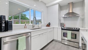 A modern kitchen with white cabinetry, stainless steel appliances, a large window, and a view of the outdoors. - 237 | Heated Pool | Putting | Outdoor Living | FreeBee Zone | by DelrayNightly (Delray Beach)