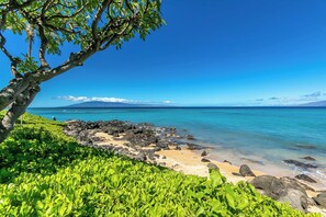 Une plage à l’eau d’un bleu cristallin, bordée d’une côte rocheuse et entourée d’une végétation luxuriante.