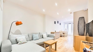 A modern living room with a grey sectional sofa, a wooden coffee table, and a dining area with a wooden table and chairs.