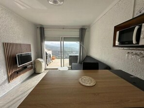A modern room with a wooden dining table, a flat-screen TV mounted on the wall, a microwave, and a balcony with a view. - Spectacular sea view studio apartment on Av-64 (Roses)