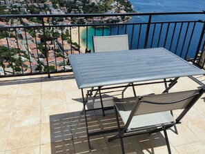 A balcony with a metal table and chairs, overlooking a coastal town and the sea. - Spectacular sea view studio apartment on Av-64 (Roses)