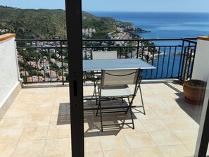A balcony with a table and chair, overlooking a coastal town and the sea. - Spectacular sea view studio apartment on Av-64 (Roses)