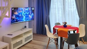 A modern living space with a staircase leading to an upper level, a flat-screen TV, a dining table with chairs, and a small table with a vase.