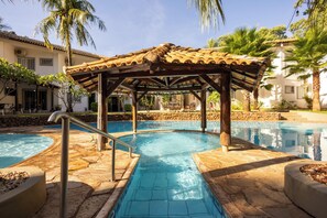Una piscina con pérgola de madera, baldosas de piedra y palmeras.