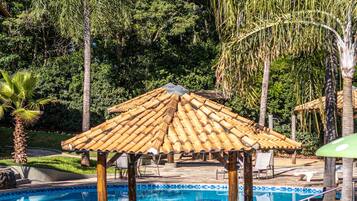 Una piscina con borde de azulejos, un pabellón de madera y palmeras circundantes.