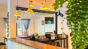 Un espace bar avec un comptoir en bois, des tabourets noirs et des lampes suspendues jaunes.