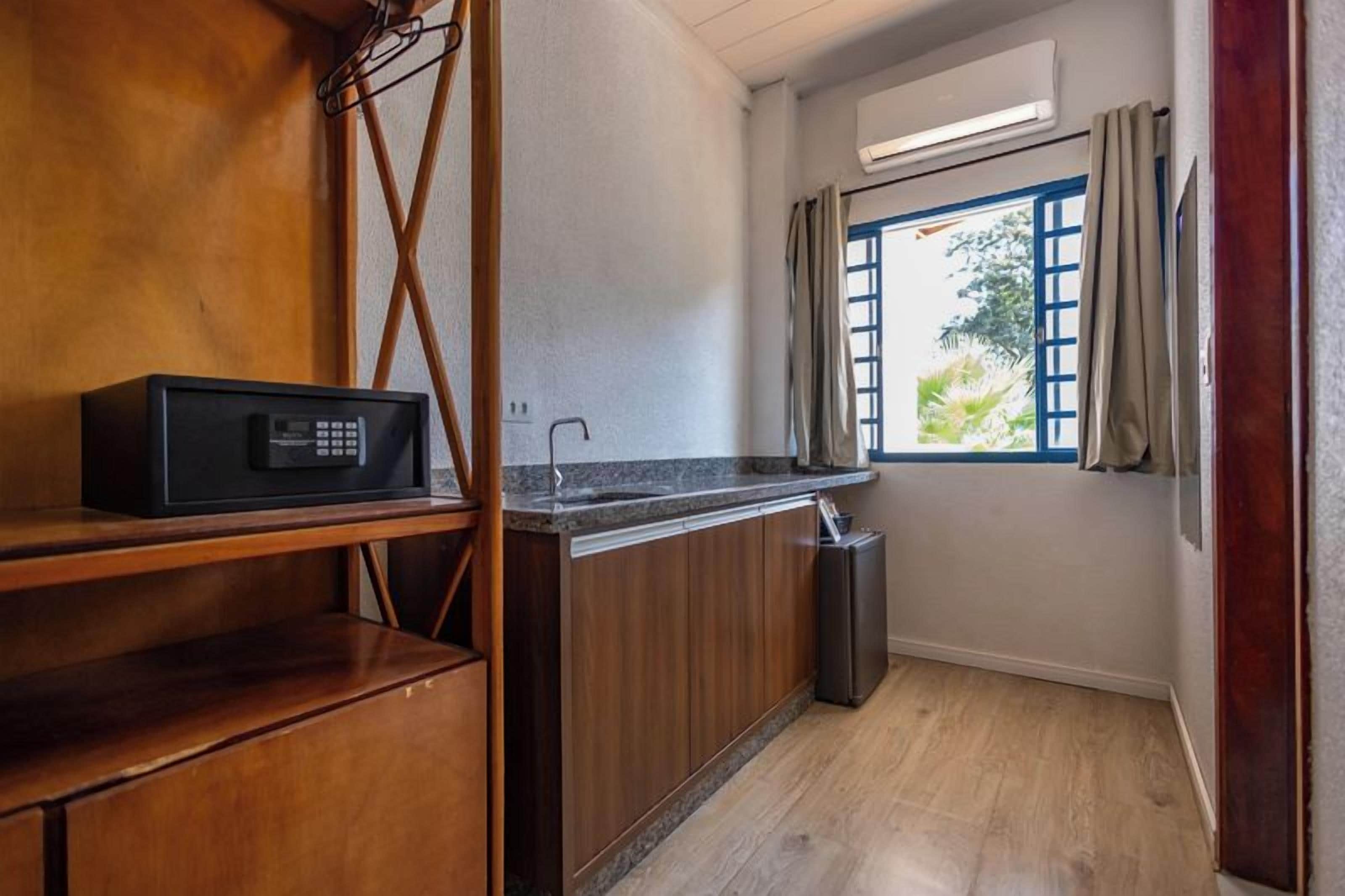 A compact kitchen with a microwave, wooden cabinets, and a window with curtains.