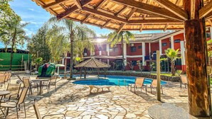A covered outdoor area with a pool, lounge chairs, and a stone-tiled floor.