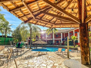 A covered outdoor area with a pool, lounge chairs, and a stone-tiled floor.