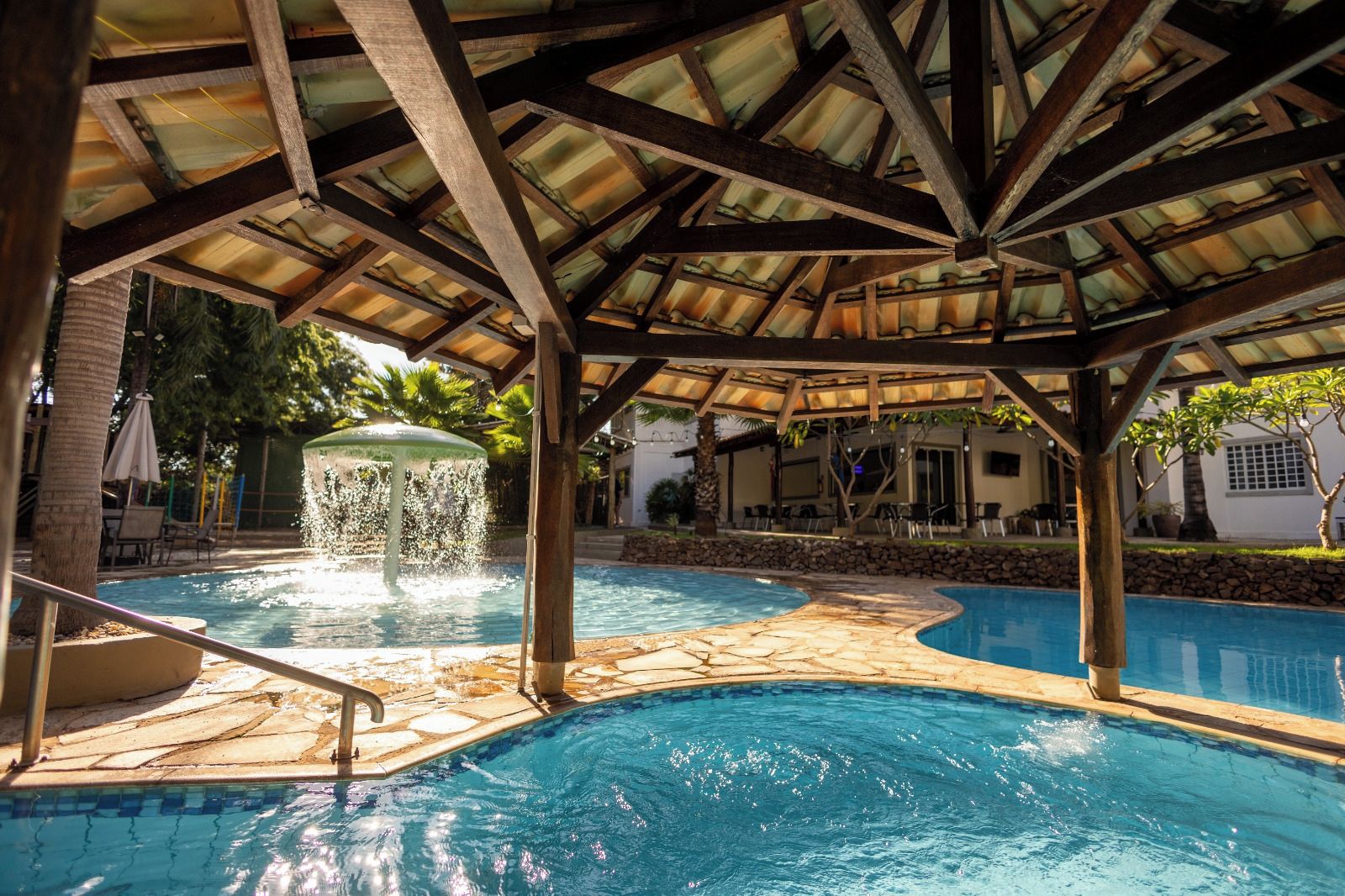 Zona de piscina con una fuente, baldosas de piedra y una estructura cubierta tipo pabellón.