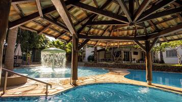 Zona de piscina con una fuente, baldosas de piedra y una estructura cubierta tipo pabellón.