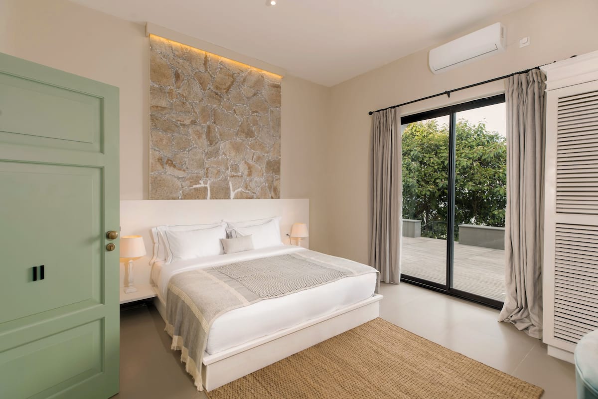 A bedroom with a large bed, a stone accent wall, a sliding glass door to the outside, and a green door.