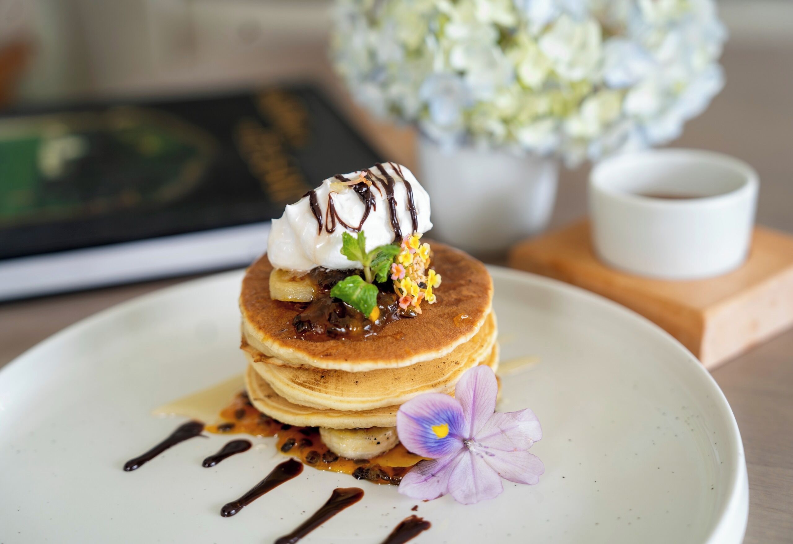 Een stapel pannenkoeken met stroop en een bloem op een bord.
