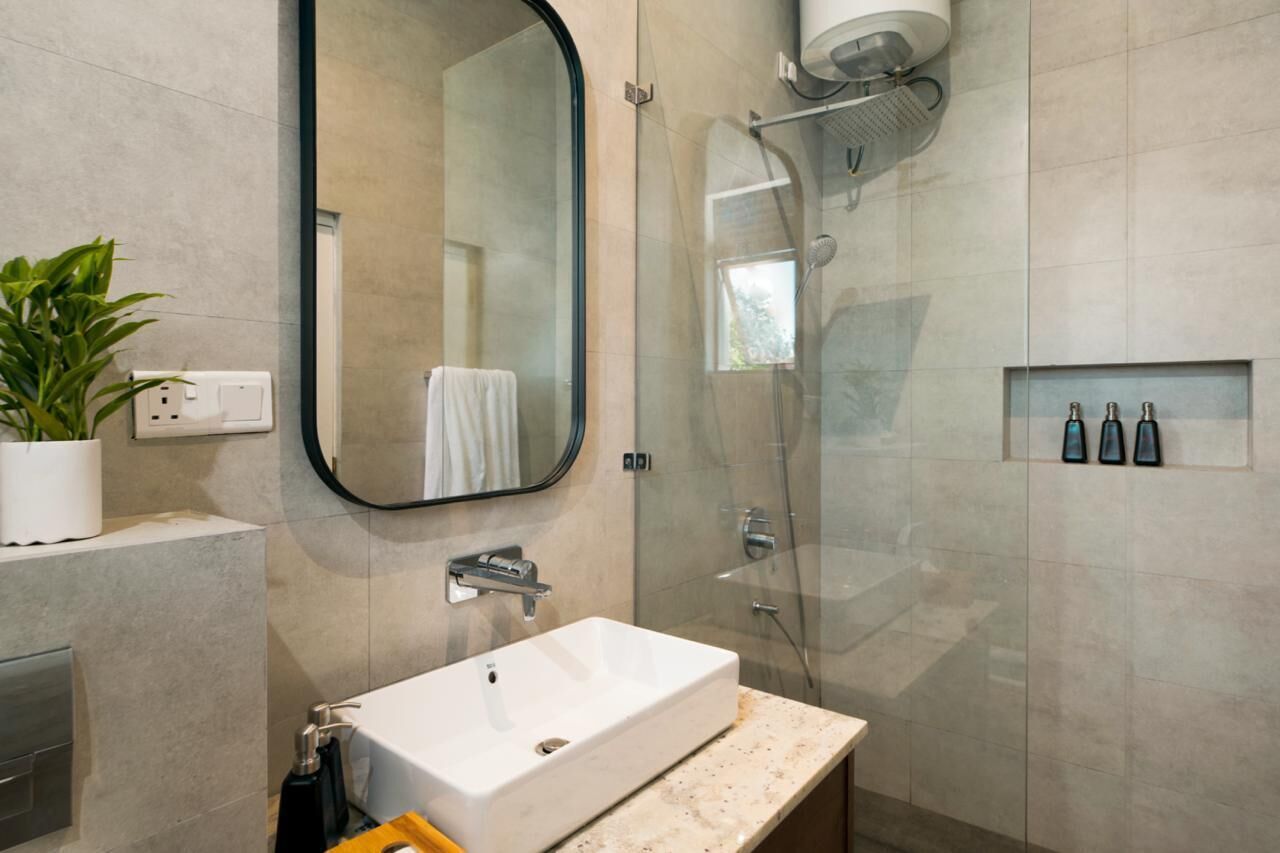 Un baño moderno con un espejo grande, un lavamanos blanco, una ducha con cerramiento de vidrio y una planta en maceta.