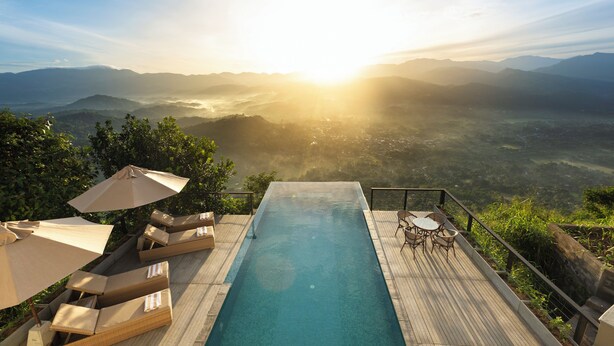 A swimming pool with lounge chairs and umbrellas, overlooking a mountainous landscape. - W15 Ambuluwawa (Gampola)