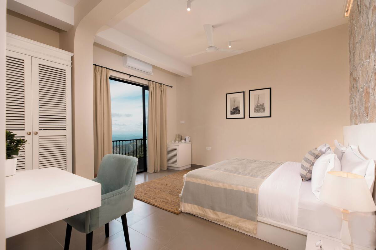 A bedroom with a bed, a desk, a chair, and a view of the outdoors.
