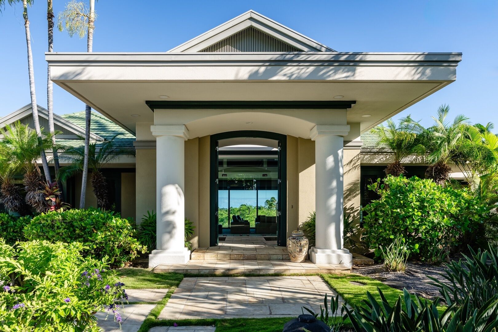 A modern house with a covered entrance, a garden with various plants, and a clear view of the sky.