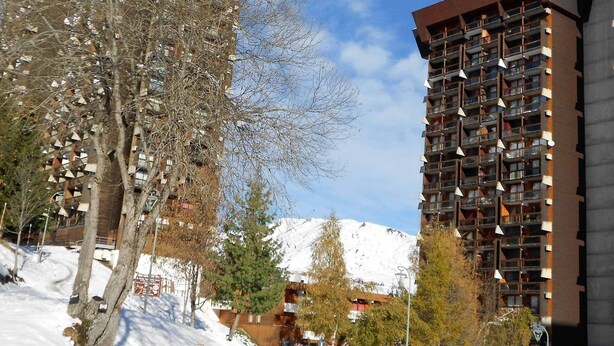 Un moderno edificio de gran altura con varios balcones y una montaña nevada al fondo.