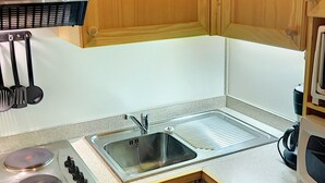 Una cocina compacta con armarios de madera, un lavamanos de acero inoxidable, un microondas y una estufa.