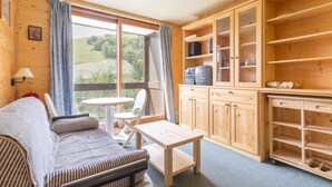Una habitación acogedora con sofá, una mesita y una zona de cocina con armarios y estanterías de madera.