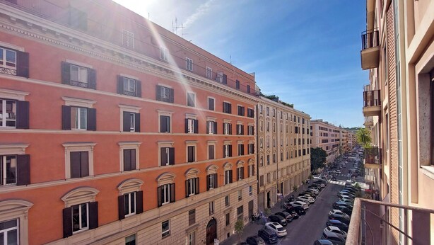 Un edificio de varios pisos con balcones y una fila de coches aparcados delante.