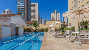 A swimming pool with lounge chairs and umbrellas, surrounded by high-rise buildings.